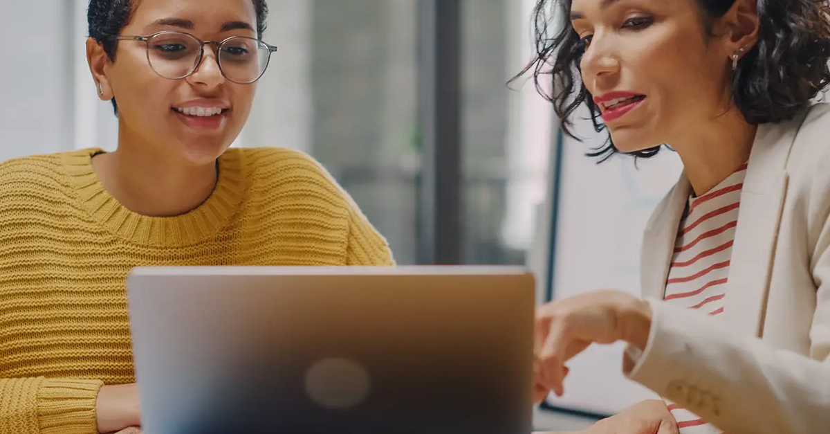 Two women review a laptop screen in meeting.