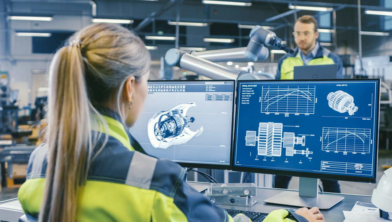 Engineer at car factory looking at car parts on computer screen.