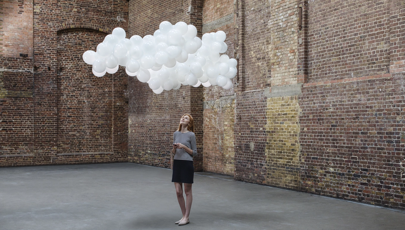 Woman standing looking at white balloons floating like a cloud.