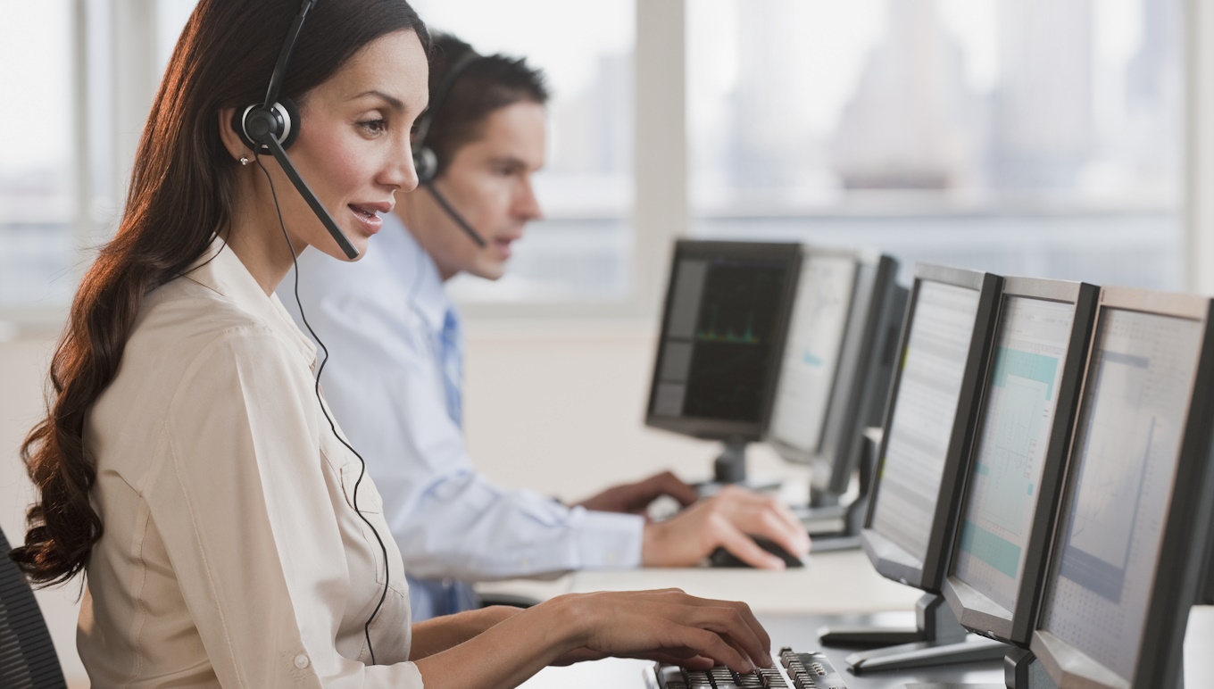 Woman and man wearing headphones and sitting in front of computer screens.