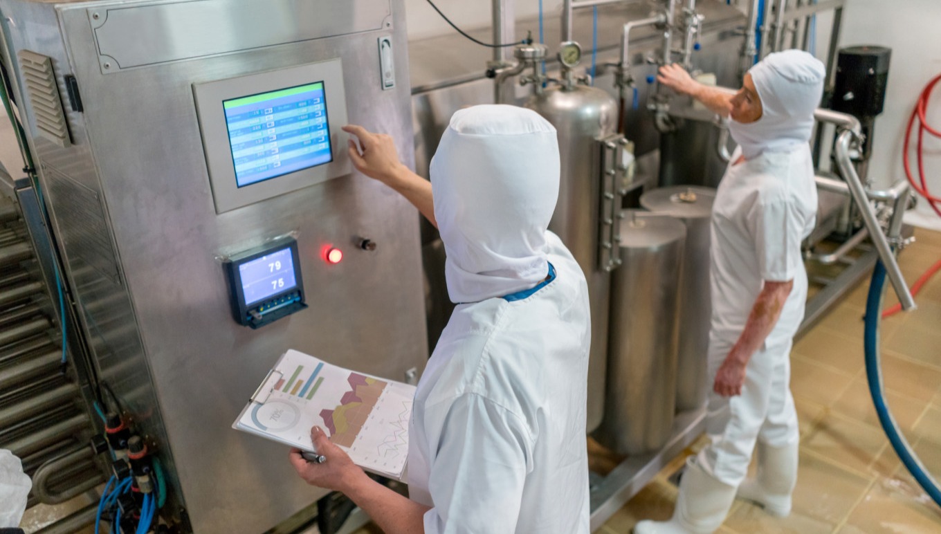 Food facility workers monitor machinery.