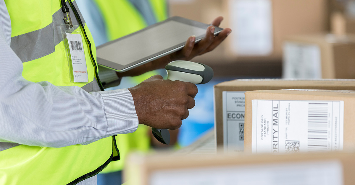 Warehouse inventory worker with RF scanner and tablet near boxes.