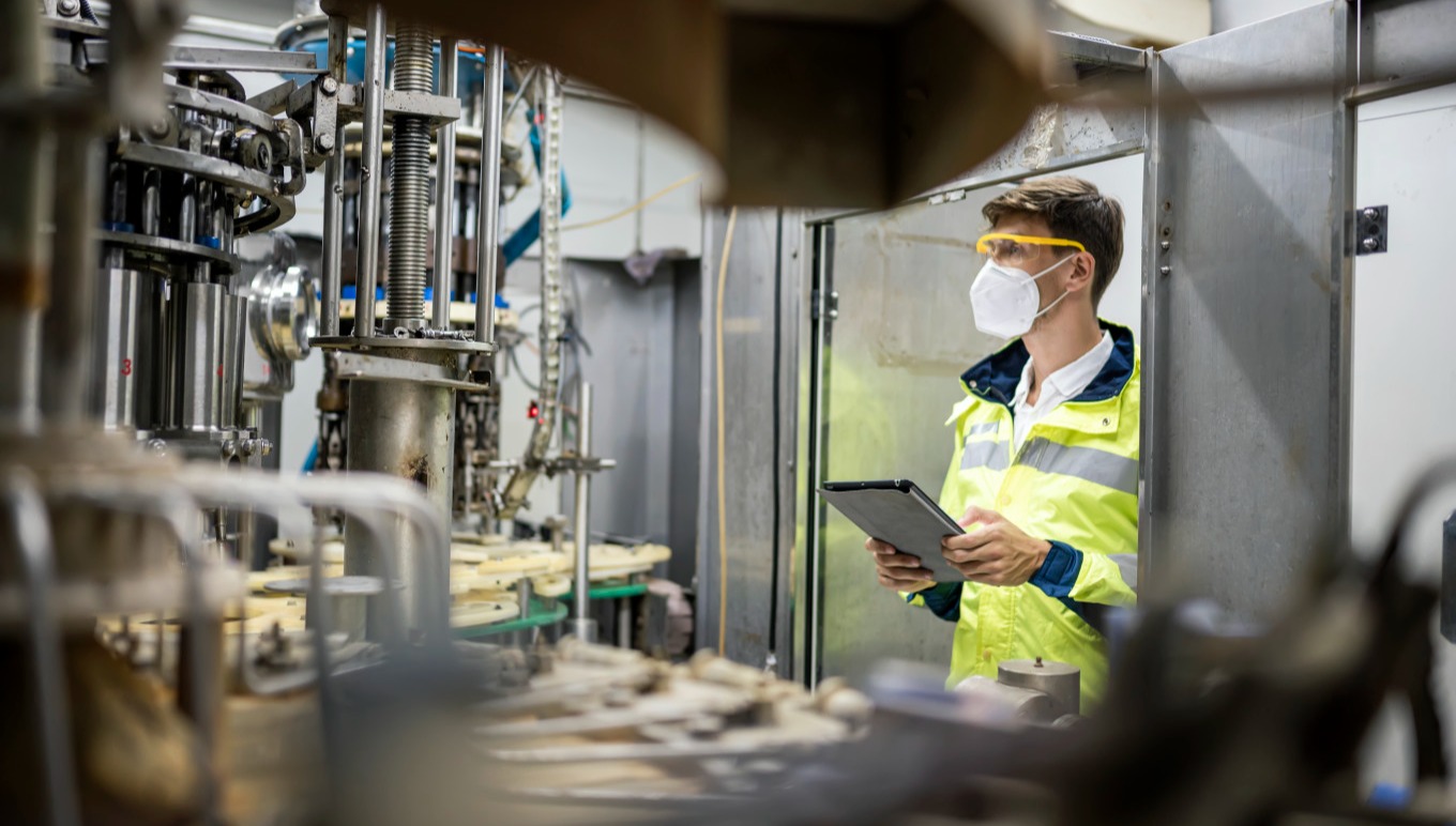 A food factory worker monitors manufacturing equipment in motion.