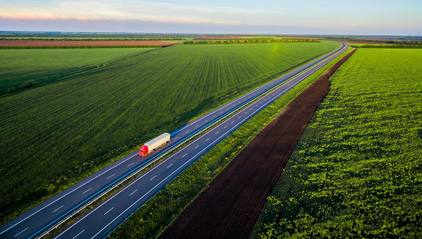 Truck driving on divided highway with green scenic fields on either side.